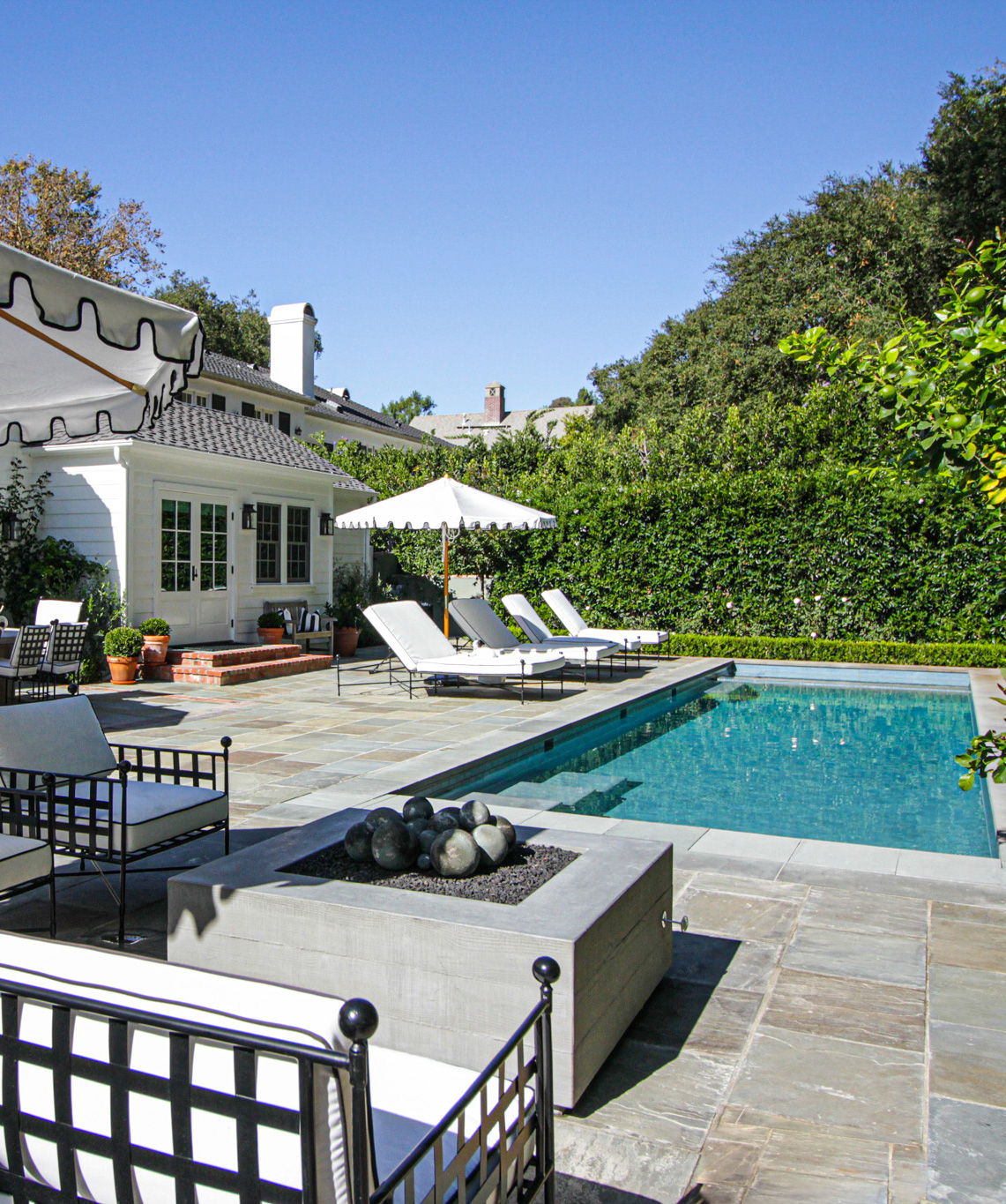 Modern poolside hardscape design in Brentwood, CA, showing an integrated spa, stone paving, and a white traditional-style home in the background.